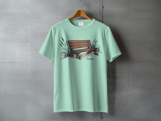 Mint green t-shirt with a drawing of a wooden bench and tall grass.