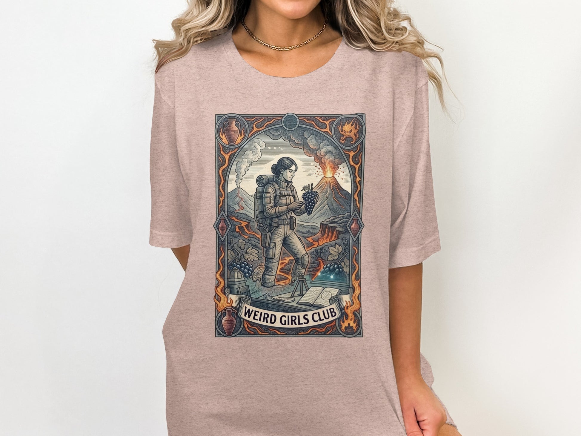 Graphic tee with volcano, woman, grapes, and text "WEIRD GIRLS CLUB".