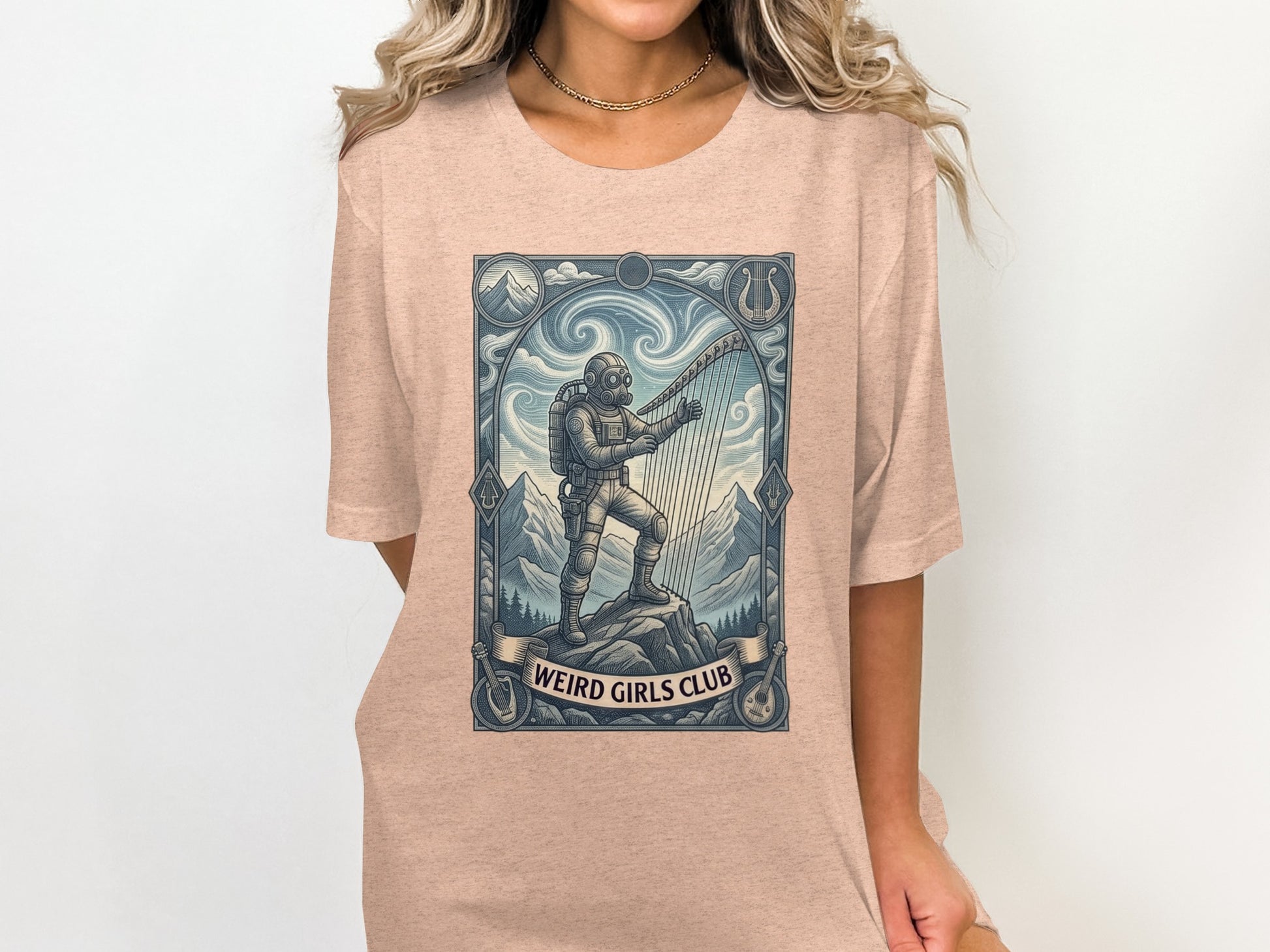 T-shirt graphic of astronaut playing harp on mountain, "Weird Girls Club" text.