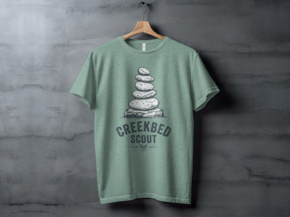 Creekbed Scout Cairn Graphic: The Explorer's Adventure Tee: T-shirt with stacked stones and "Creekbed Scout" text on a hanger.