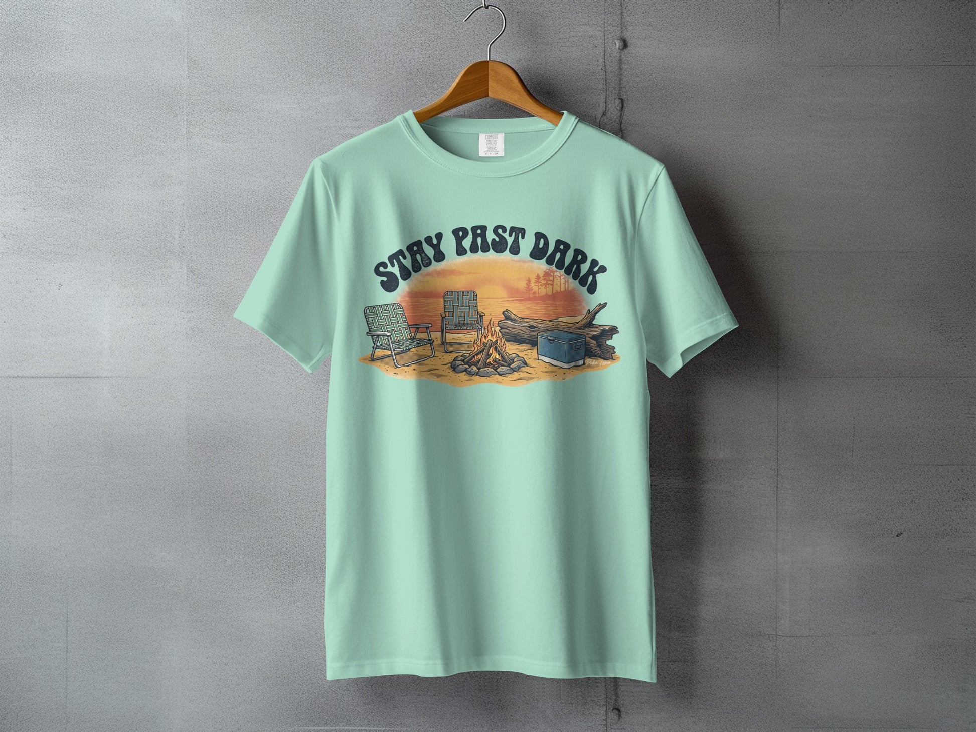 Mint t-shirt with "STAY PAST DARK" text over campfire scene with chairs.