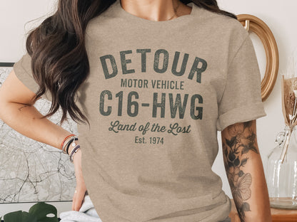 Tan t-shirt with "DETOUR MOTOR VEHICLE C16-HWG Land of the Lost Est. 1974" text.