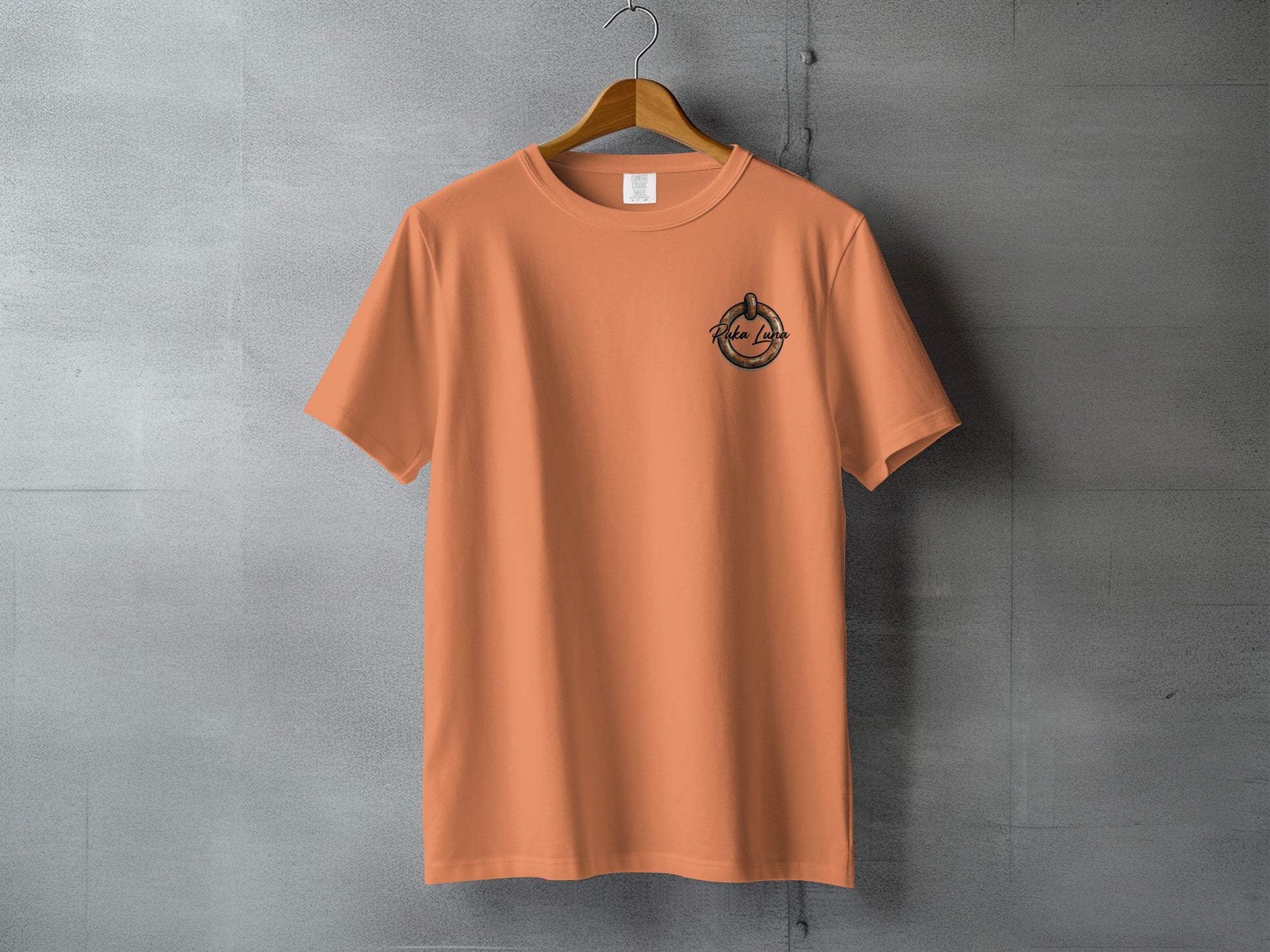 Orange t-shirt with "Falsa Luce" logo on gray concrete wall.