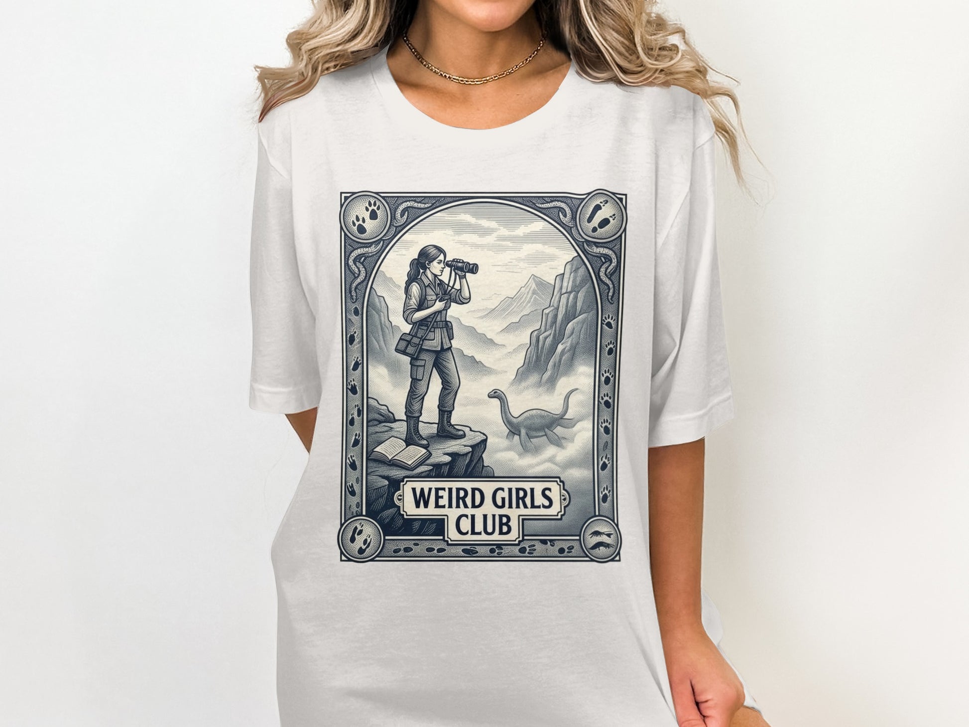 T-shirt featuring "Weird Girls Club" logo with woman in mountains and dinosaur.