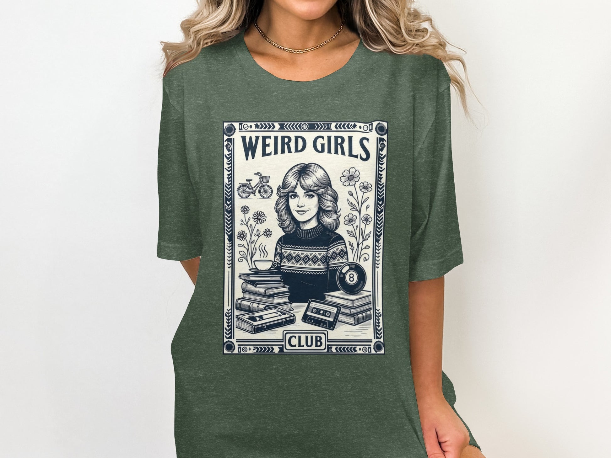 Dark green t-shirt with "Weird Girls Club" graphic featuring a woman, books, and cassette tape.