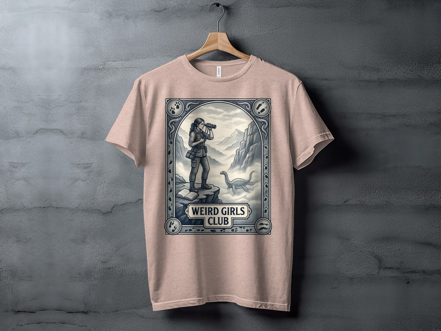 Pink t-shirt with "Weird Girls Club" logo featuring a woman with binoculars and a dinosaur.