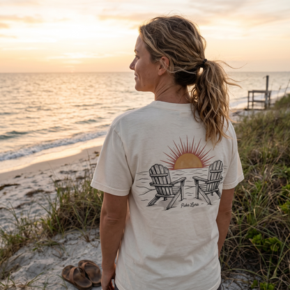 Woman wearing a cream t-shirt with a sunset graphic on a beach.