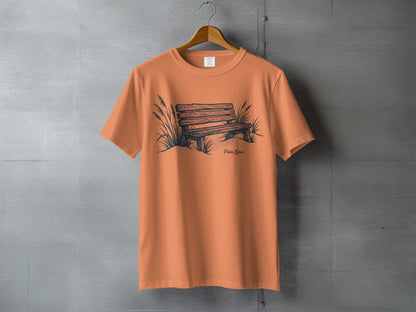 Orange t-shirt with a sketch of a park bench and grass.