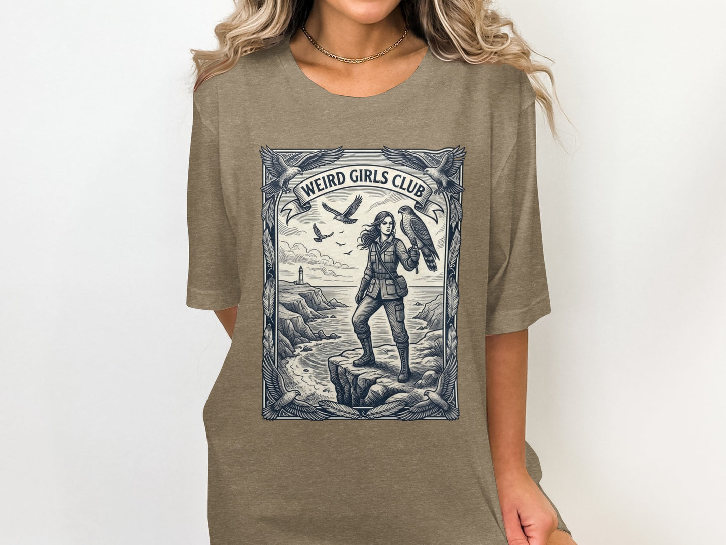 Woman in t-shirt with "Weird Girls Club" graphic of woman with hawk on cliff.