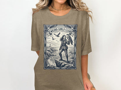 Woman in t-shirt with "Weird Girls Club" graphic of woman with hawk on cliff.