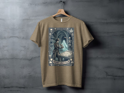 Brown t-shirt with "Weird Girls Club" text and spooky illustration.