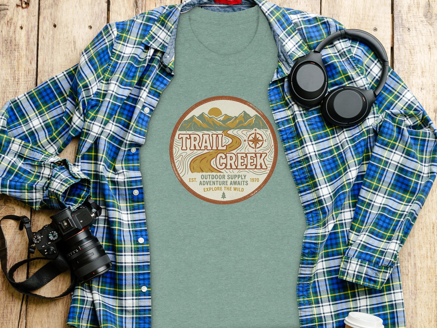 Heritage Heritage Explorer Trail Creek Nomad Tee: T-shirt with "Trail Creek Outdoor Supply Adventure Awaits Explore The Wild" circular logo, headphones, and camera.