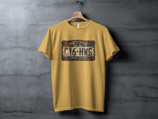 Land of the Lost Detour Plate: The Explorer's Adventure Tee: Mustard t-shirt with "DETOUR EST. 1955 C16-HWG LAND OF THE LOST" license plate graphic.