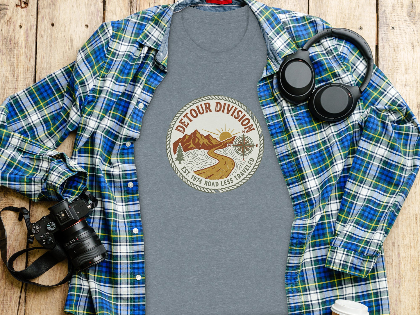 Detour Division Heritage | Vintage Outdoor Apparel: Grey t-shirt with "Detour Division" logo, plaid shirt, camera, and headphones.