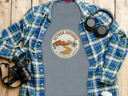Detour Division Heritage | Vintage Outdoor Apparel: Grey t-shirt with "Detour Division" logo, plaid shirt, camera, and headphones.