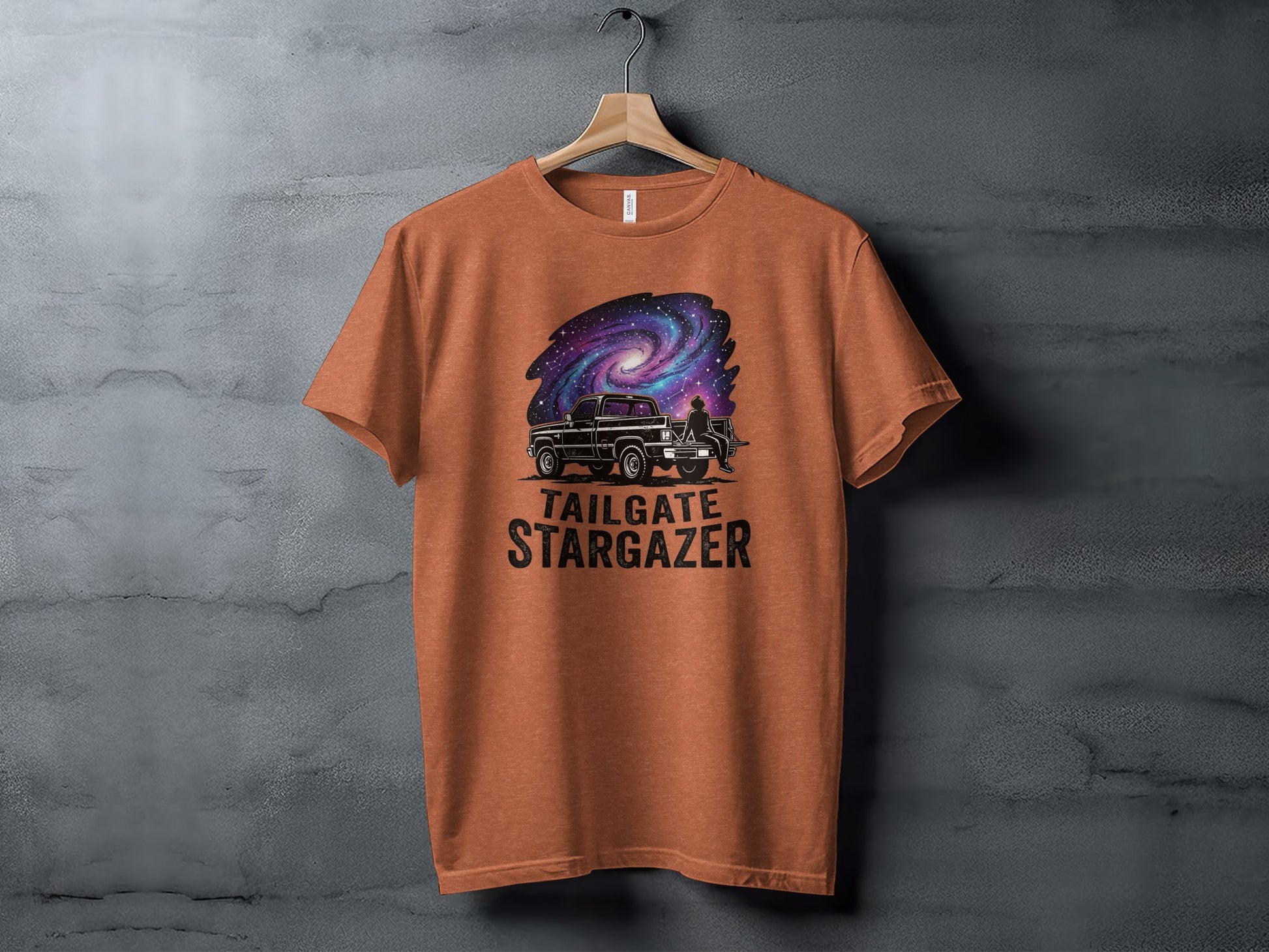 Heritage Cosmic Tailgate Stargazer Nomad Tee: Orange t-shirt with truck, person, and galaxy graphic, text "TAILGATE STARGAZER".