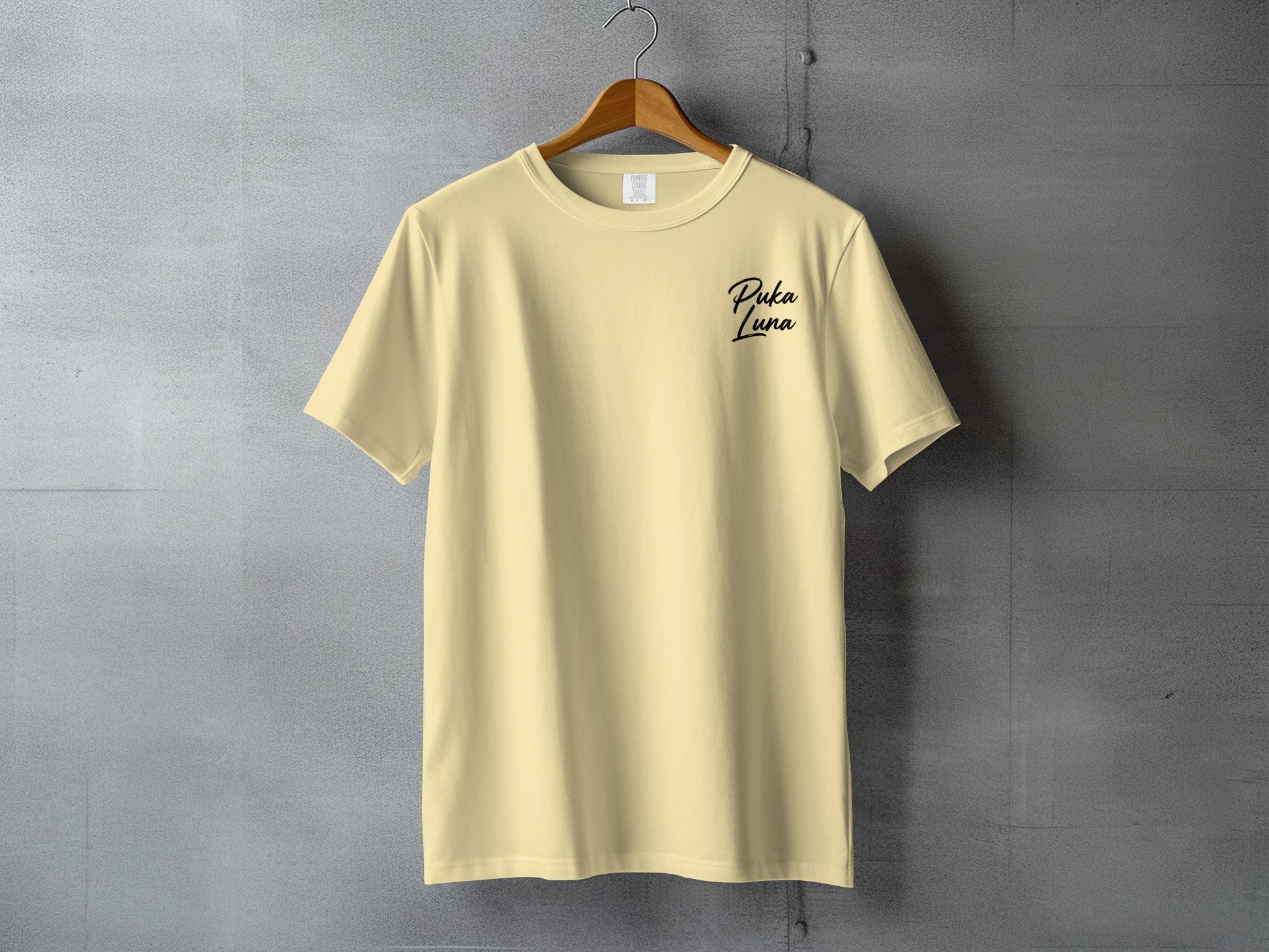 Cream t-shirt with "Puka Luna" text logo on the chest, hanging on a hanger.