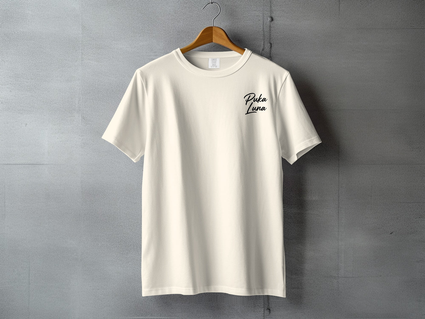 Cream t-shirt hanging on a gray textured wall with "Puka Luna" text.