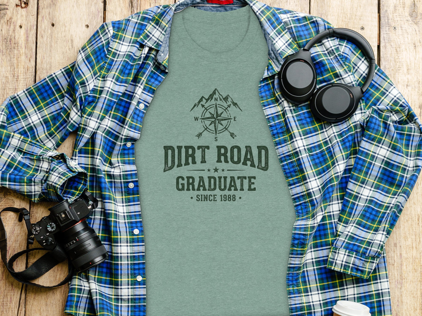 The Original Dirt Road Graduate Outdoor Adventure Top: Green t-shirt with "Dirt Road Graduate Since 1988" text, headphones, and camera.