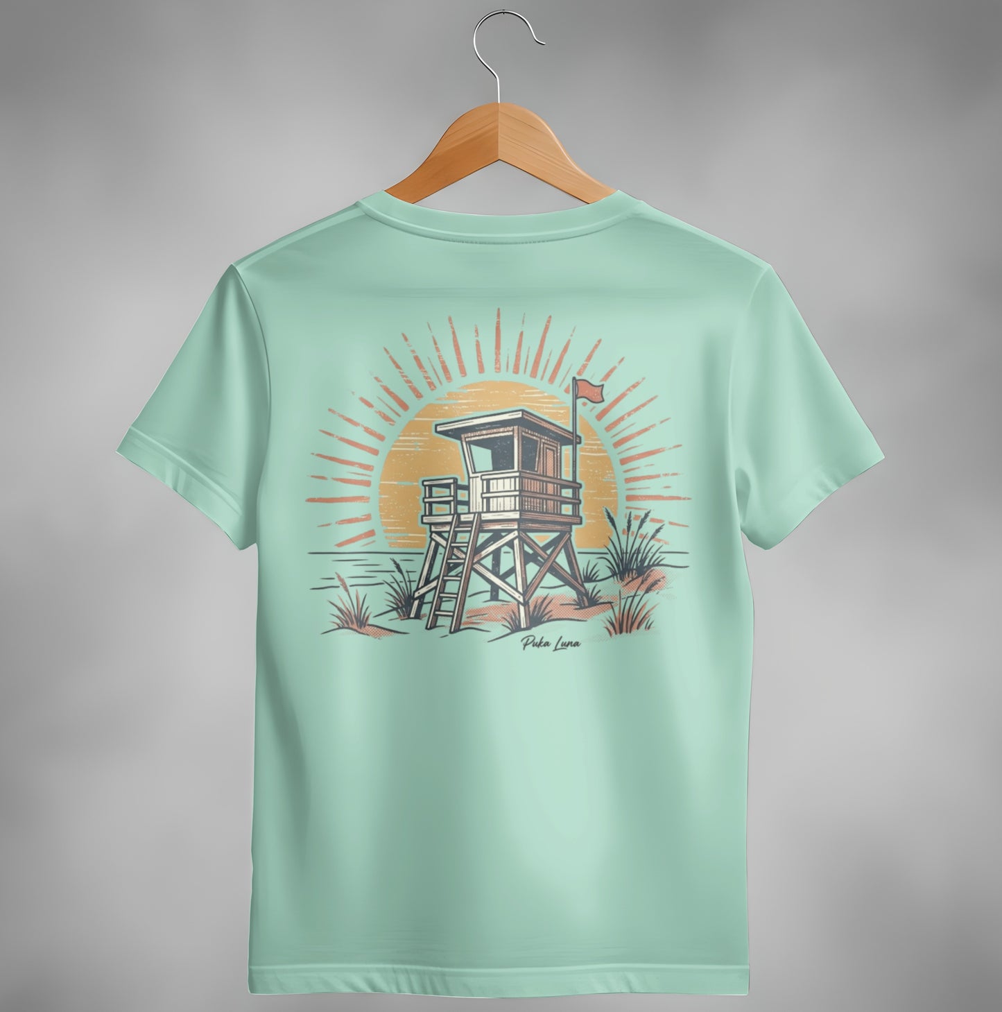 Beach lifeguard tower with sun and ocean waves graphic on light green t-shirt.