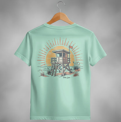 Beach lifeguard tower with sun and ocean waves graphic on light green t-shirt.