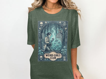 Woman in lab coat examines mushrooms near a tombstone with "CRYPT" on a t-shirt.