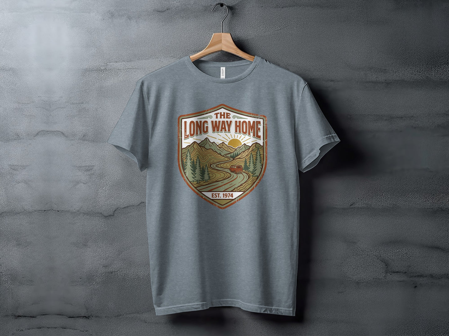 Rugged The Long Way Home | Vintage Adventure Wilderness Shirt: Grey t-shirt with a distressed shield graphic featuring a sun, mountains, and a car.