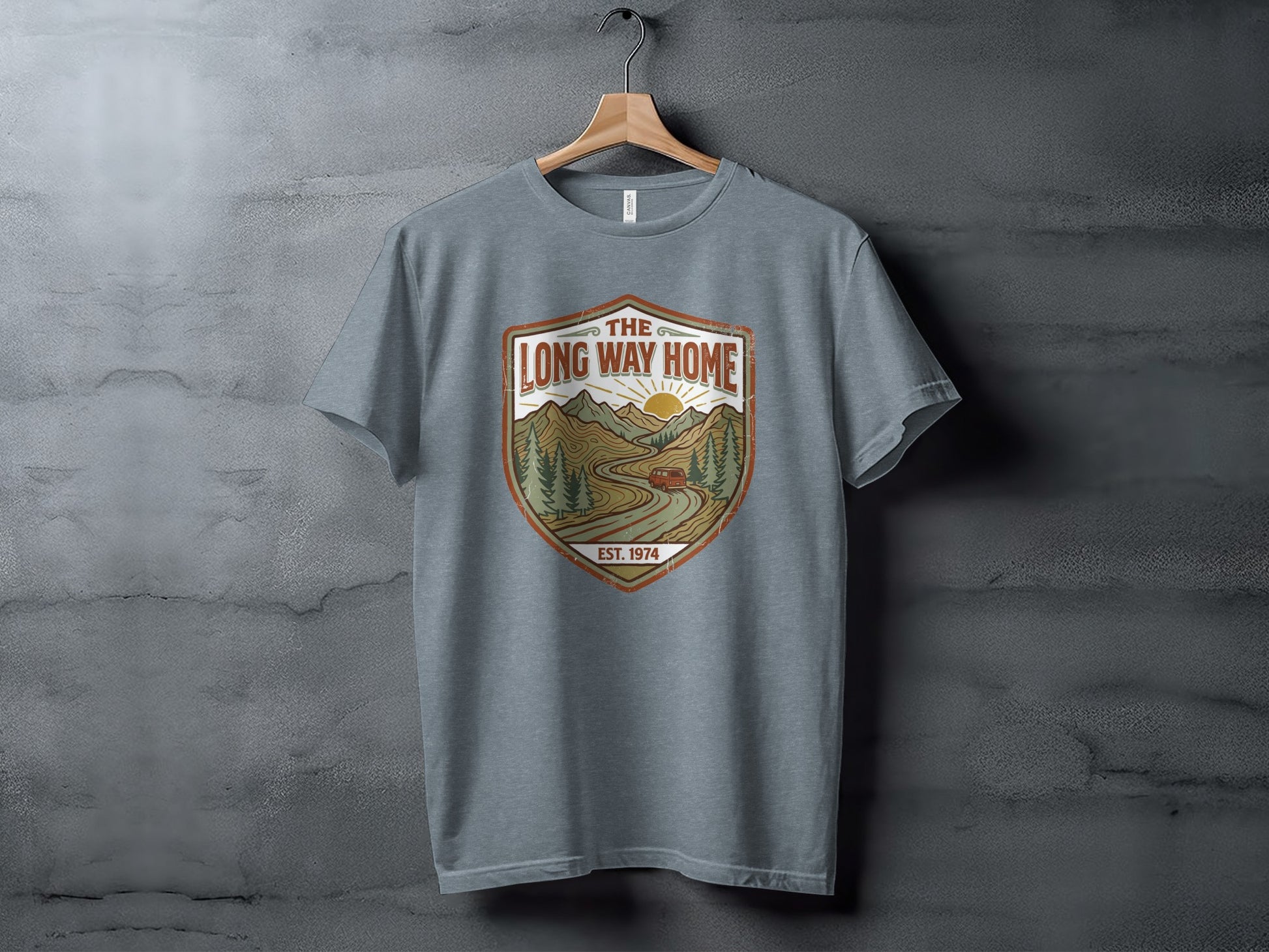 Rugged The Long Way Home | Vintage Adventure Wilderness Shirt: Grey t-shirt with a distressed shield graphic featuring a sun, mountains, and a car.