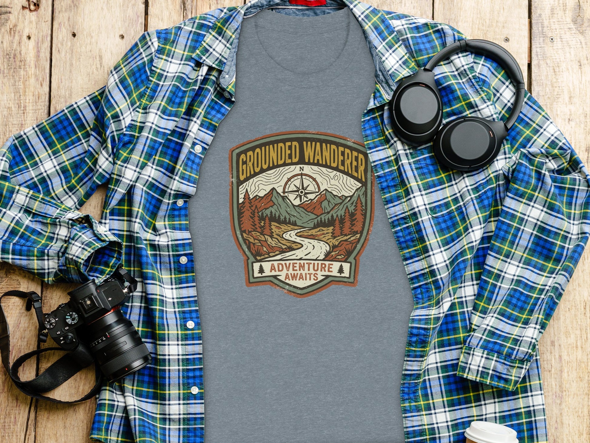Heritage Grounded Wanderer Adventure Nomad Tee: Gray t-shirt with "Grounded Wanderer Adventure Awaits" nature graphic, laid flat with headphones.