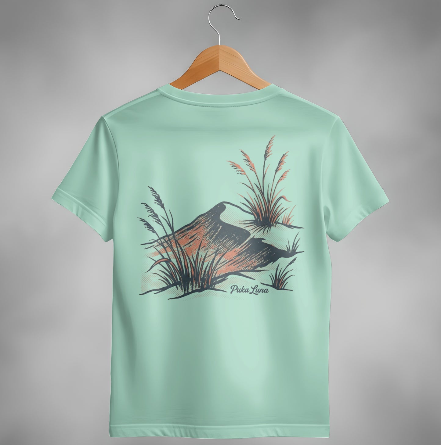 Mint green t-shirt with abstract mountain and grass design and "Puka Luna" text.
