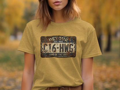 Land of the Lost Detour Plate: The Explorer's Adventure Tee: Yellow t-shirt with distressed "Detour EST 1955 C16-HWG Land of the Lost" license plate graphic.