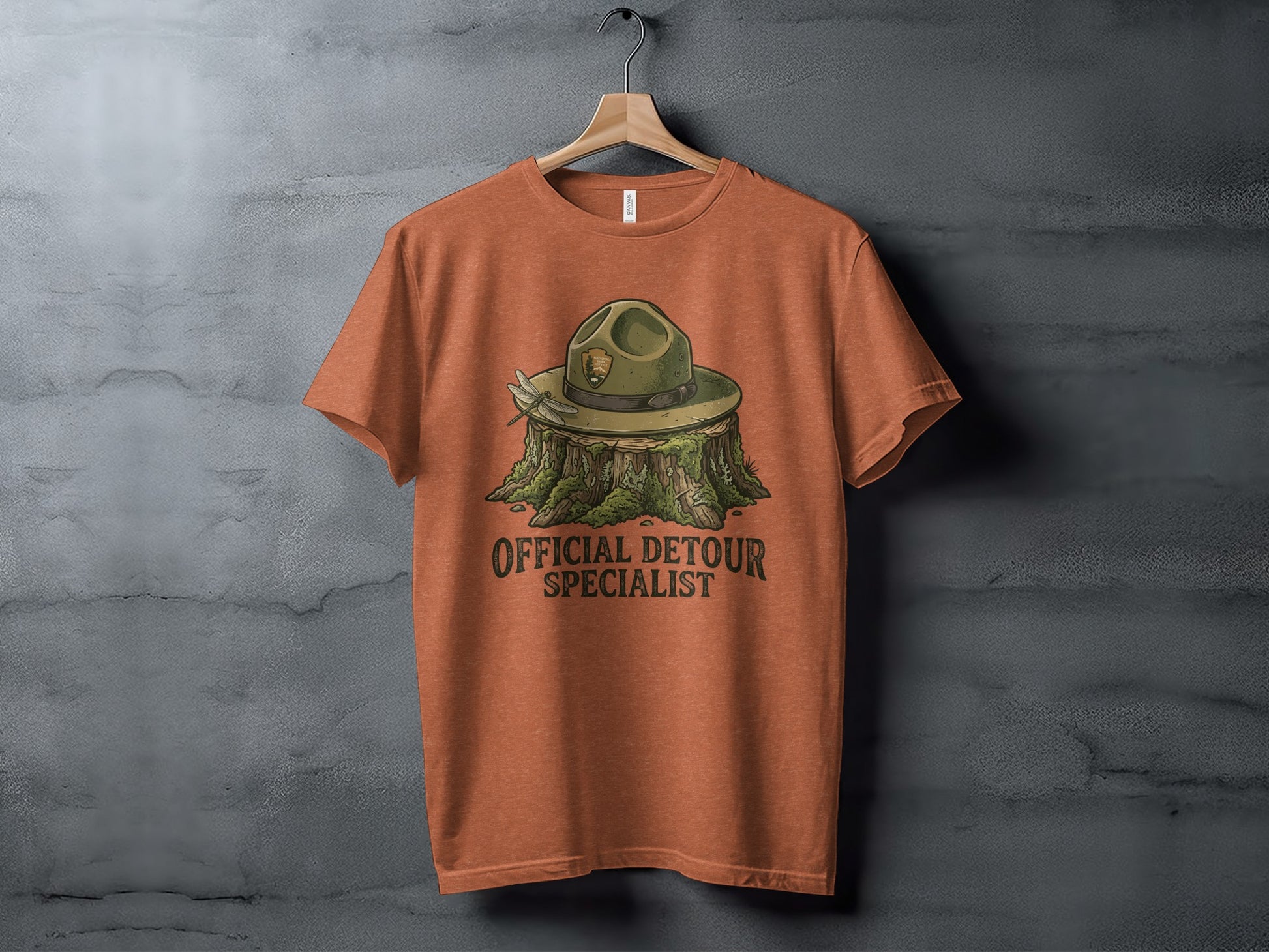Official Detour Specialist Heritage | Vintage Outdoor Apparel: Orange t-shirt with ranger hat on a stump, "Official Detour Specialist" text.