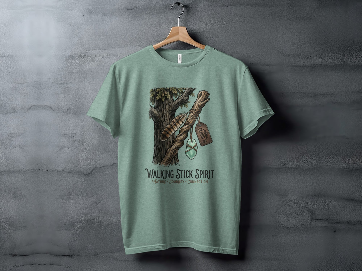 Heritage Walking Stick Spirit: Journey Nomad Tee: Green t-shirt with a nature-inspired graphic of a feather and gem on a tree branch.