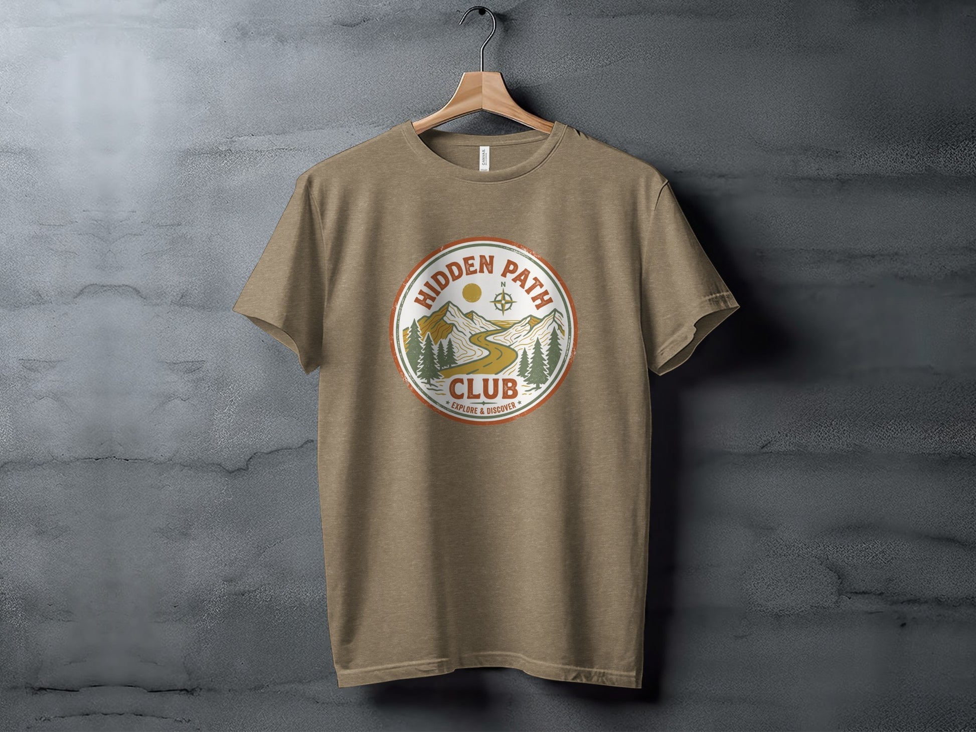 Rugged Hidden Path Club Explorer Wilderness Shirt: Brown t-shirt with circular "Hidden Path Club" logo featuring mountains, trees, and compass.