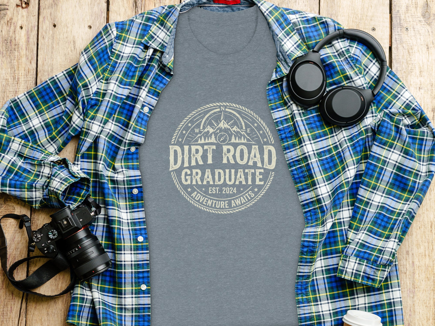 Dirt Road Graduate '24 Adventure | Vintage Outdoor Apparel: Gray t-shirt with "Dirt Road Adventure Awaits" graphic, spread open with headphones and camera.