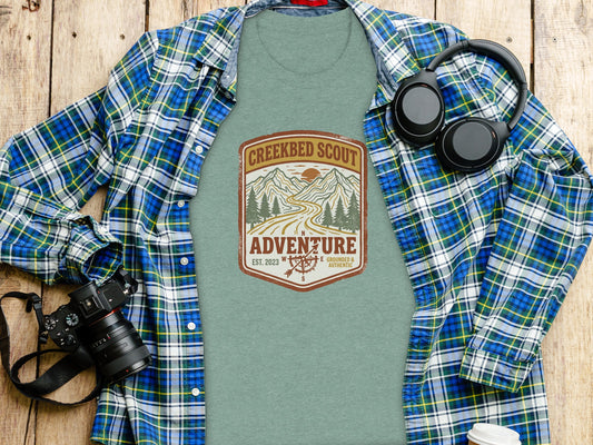 Rugged Creekbed Scout Adventure Emblem Wilderness Shirt: Green t-shirt with "Creekbed Scout Adventure" logo, headphones, and camera.
