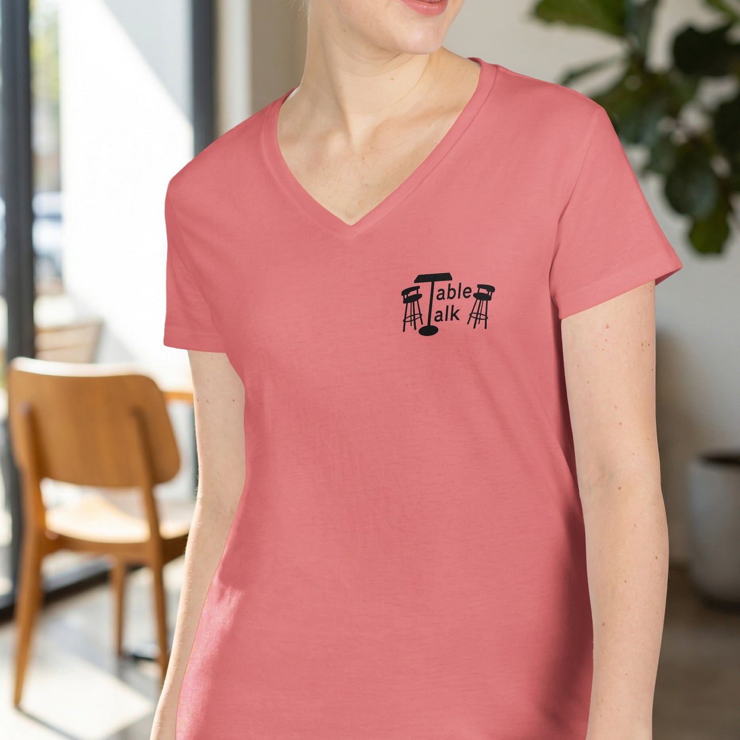 Salmon pink v-neck t-shirt with "Table Talk" logo and stools.