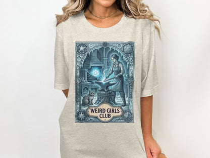T-shirt with a woman blacksmithing with a cat beside her, "Weird Girls Club" text.