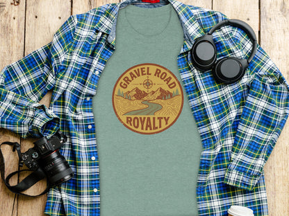 Gravel Road Royalty Adventure Tee | Vintage Outdoor Apparel: T-shirt with "Gravel Road Royalty" mountain scene design, spread out with headphones and camera.
