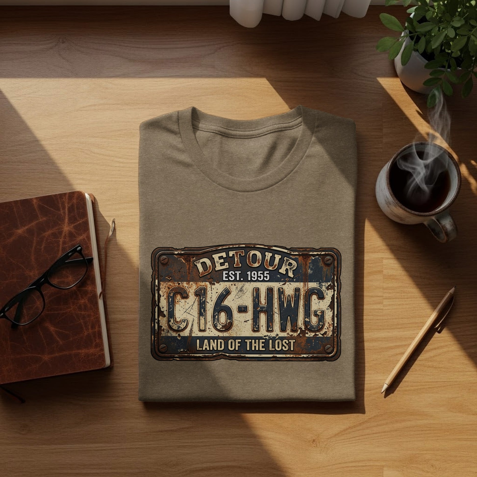 Land of the Lost Detour Plate: The Explorer's Adventure Tee: Taupe t-shirt with "Detour Est. 1955 C16-HWG Land of the Lost" license plate graphic.