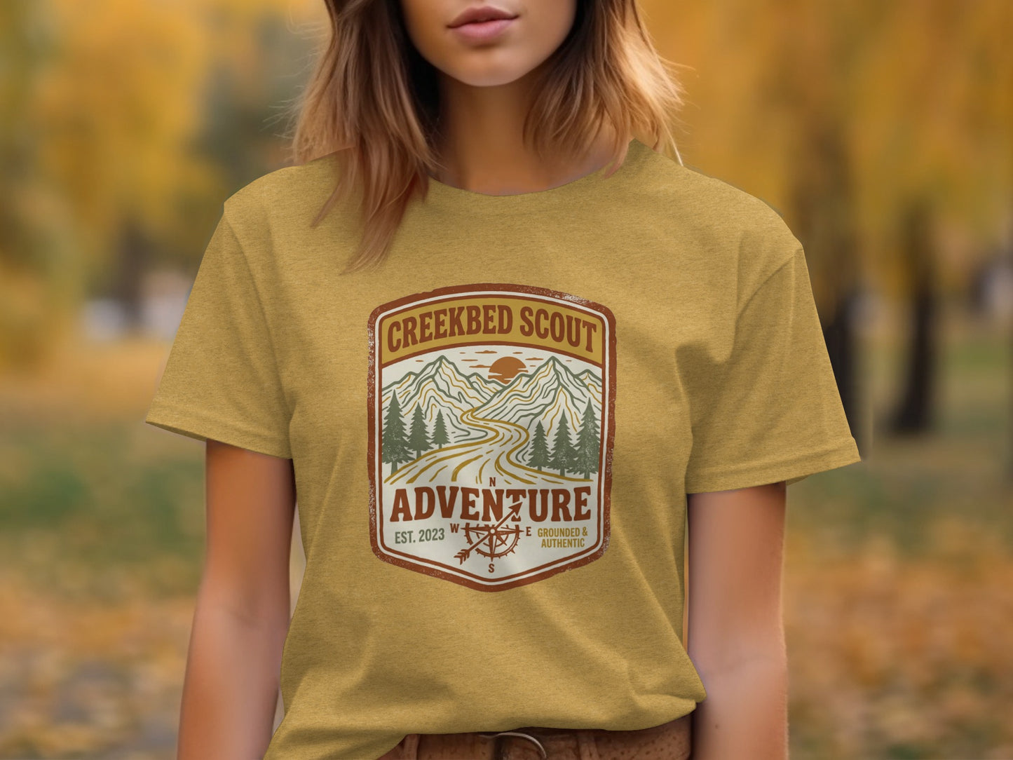 Rugged Creekbed Scout Adventure Emblem Wilderness Shirt: Yellow t-shirt with "Creekbed Scout" logo featuring mountains and compass.