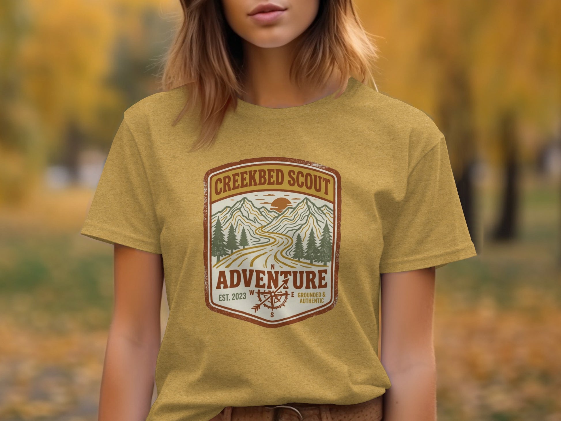 Rugged Creekbed Scout Adventure Emblem Wilderness Shirt: Yellow t-shirt with "Creekbed Scout" logo featuring mountains and compass.