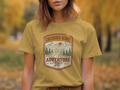 Rugged Creekbed Scout Adventure Emblem Wilderness Shirt: Yellow t-shirt with "Creekbed Scout" logo featuring mountains and compass.