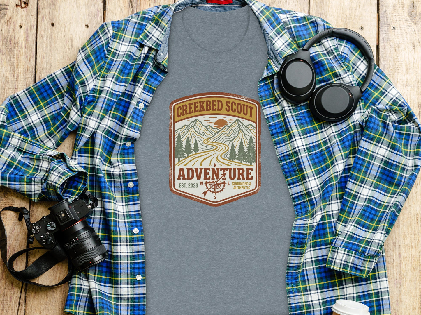 Rugged Creekbed Scout Adventure Emblem Wilderness Shirt: Grey t-shirt with "Creekbed Scout Adventure" logo, laid on a wooden surface.