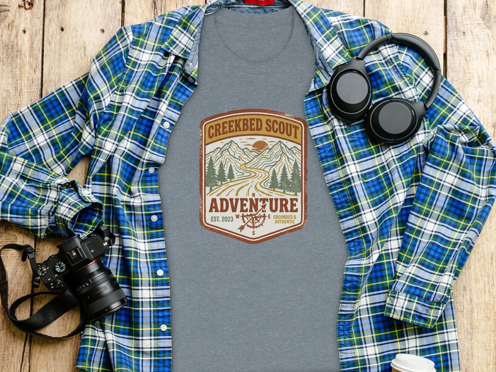 Rugged Creekbed Scout Adventure Emblem Wilderness Shirt: Grey t-shirt with "Creekbed Scout Adventure" logo, laid on a wooden surface.