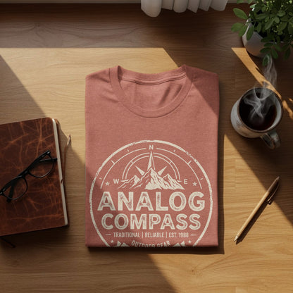 Analog Compass Heritage: The Explorer's Adventure Tee: Pink t-shirt with Analog Compass logo and text, on a wooden surface.