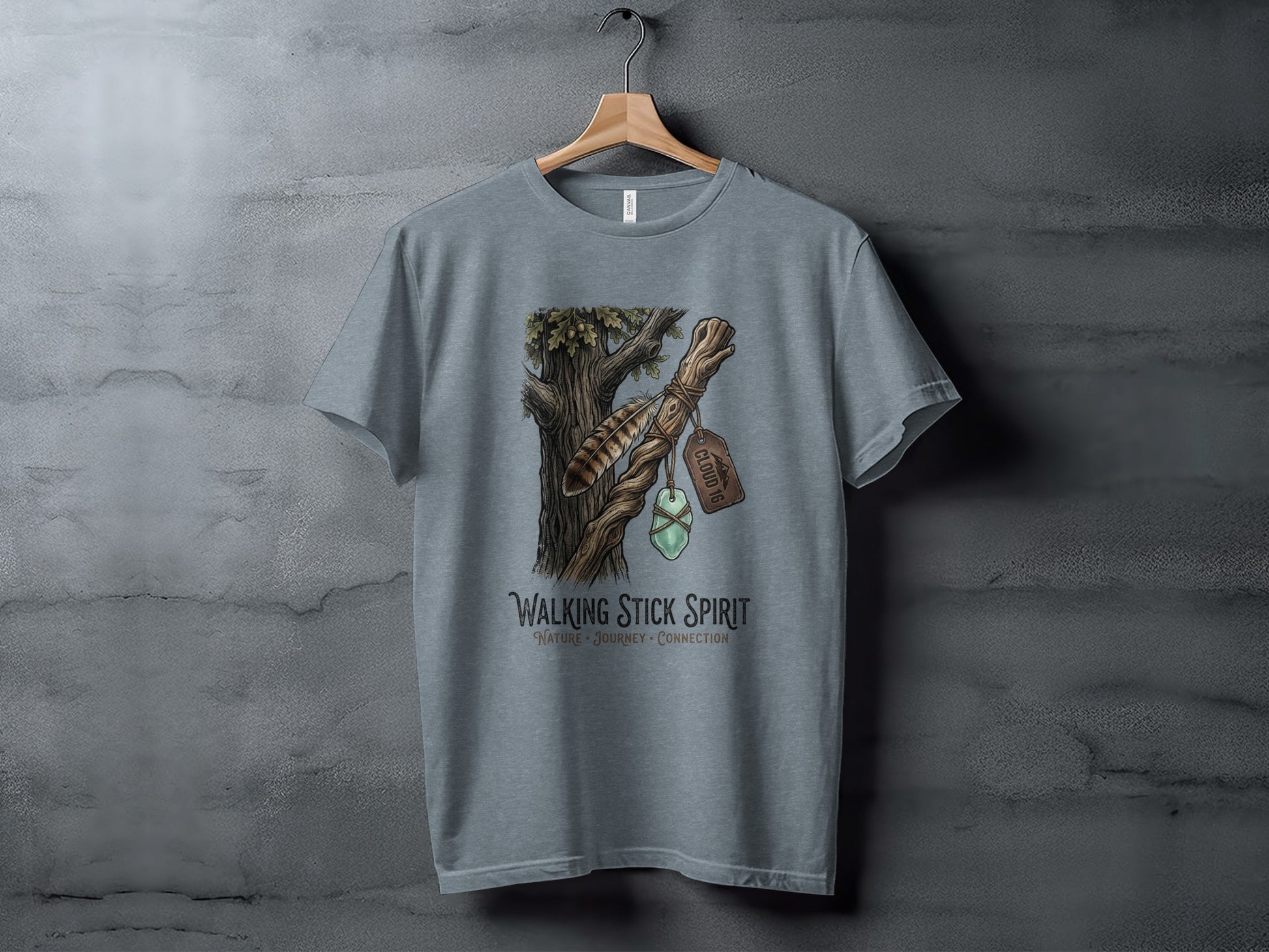 Heritage Walking Stick Spirit: Journey Nomad Tee: Grey t-shirt with a nature-themed design featuring a walking stick and feather.