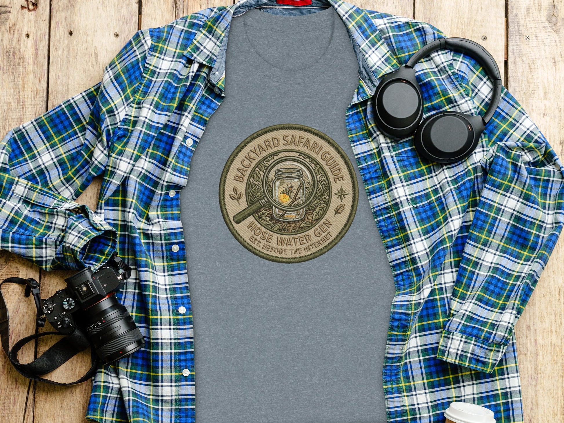 Backyard Safari Guide Explorer: Backcountry Outpost Shirt: T-shirt with "Backyard Safari Guide" circular logo, layed flat with camera and headphones.