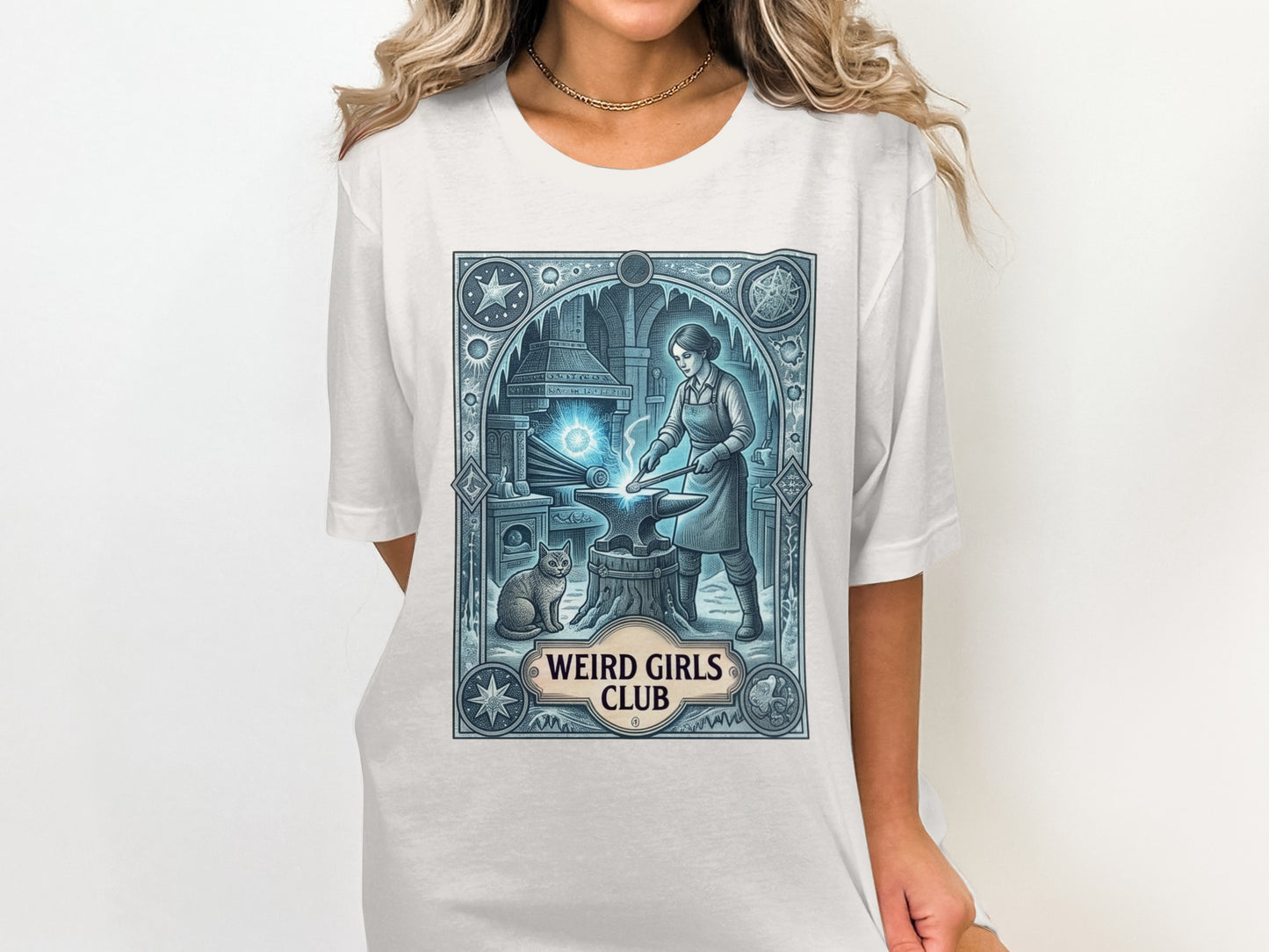T-shirt graphic with a woman blacksmithing next to a cat, "Weird Girls Club" text.