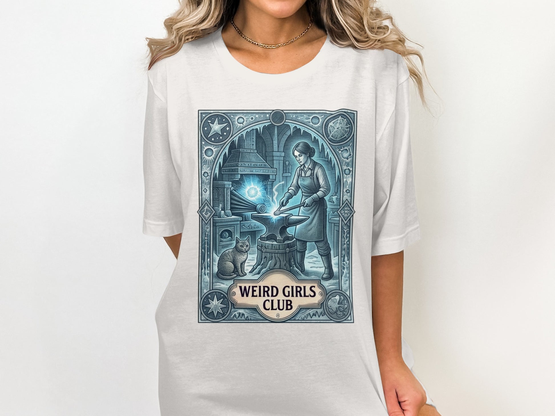 T-shirt graphic with a woman blacksmithing next to a cat, "Weird Girls Club" text.